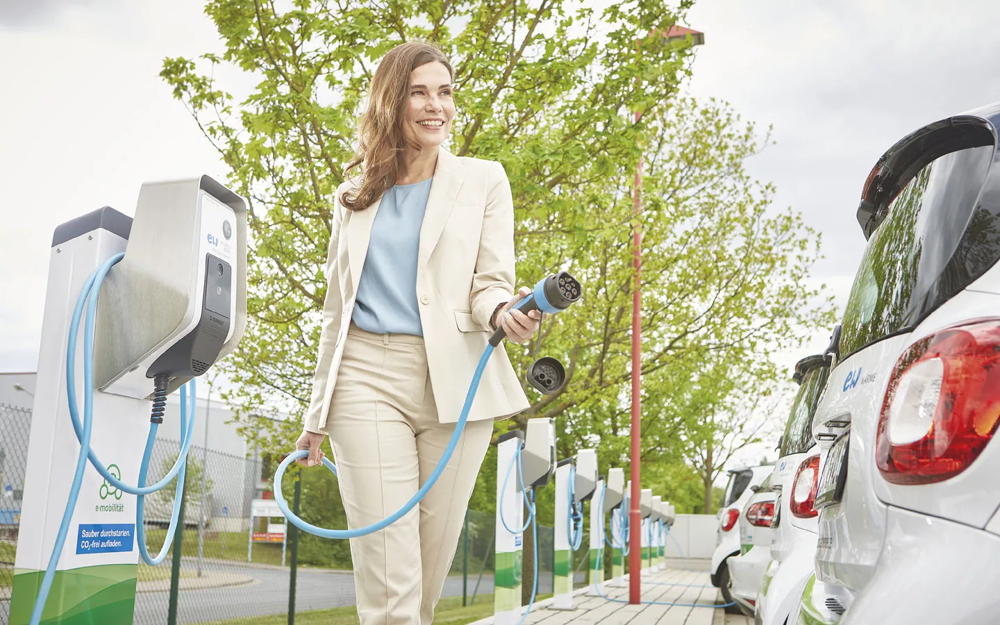 E-Mobilität - Kundin vor Ladestation mit Stecker in der Hand · Degen